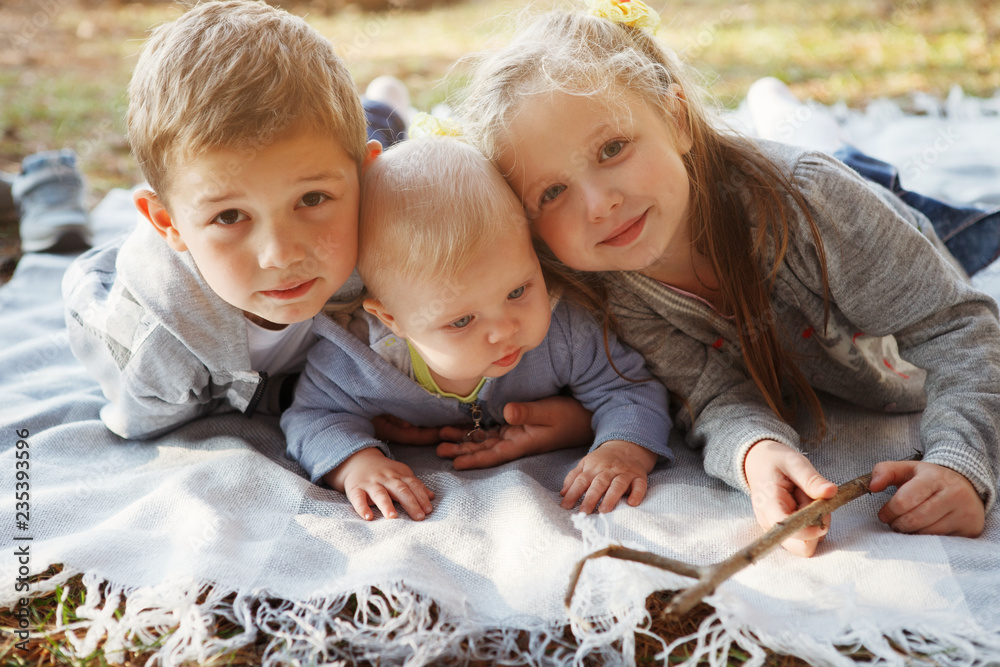 Φωτογραφία Three children, elder brother, sister blonde and 7-month-old boy with blue eyes are lying on a rug in the autumn forest