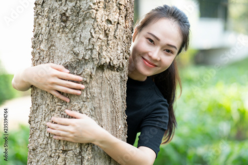 Close-up of a smiling asian young woman hugging tree at the park