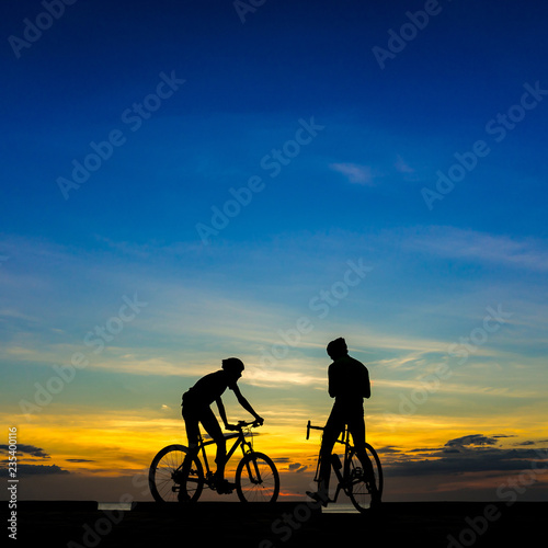 Cyclists with bicycles at the beach, at dusk.