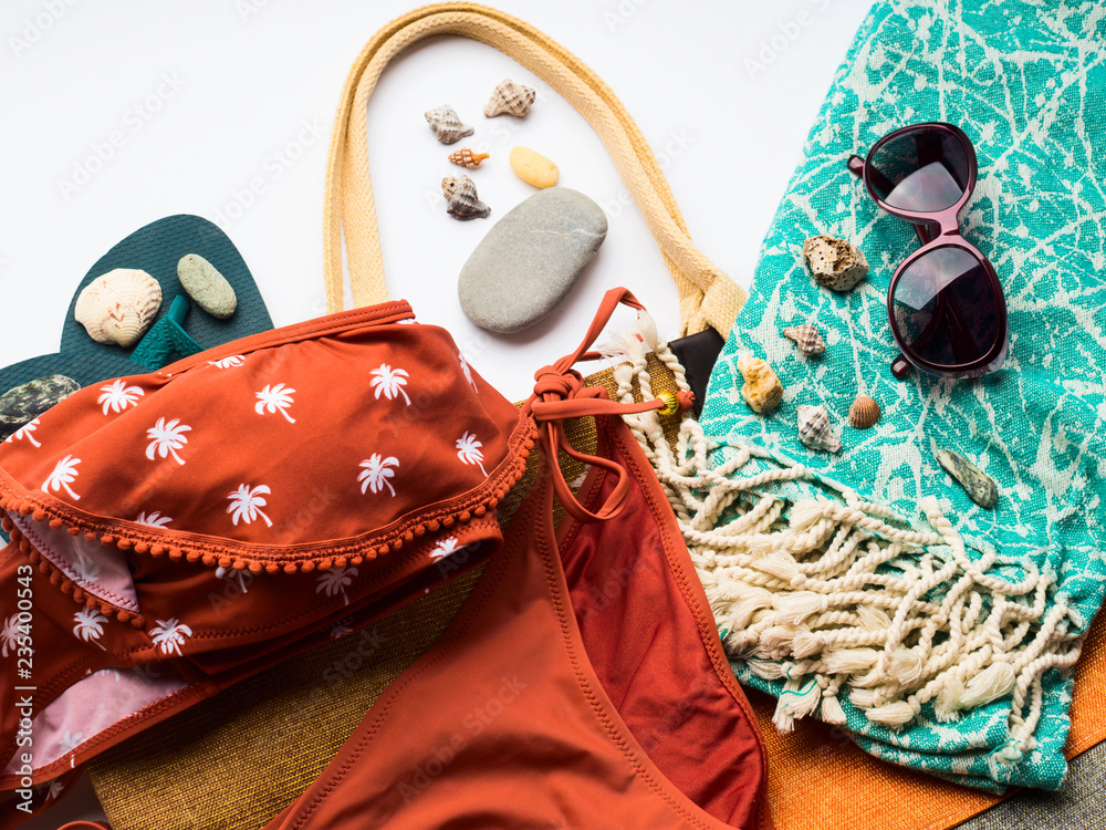 Fototapeta premium Beach female fashion accessories swimsuit, sun glasses, hat, flip flops, towel and bag. Summer traveling holiday concept flat lay