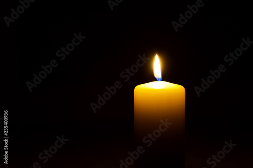 One yellow candle flame burning in darkness on black background with copy space for text.