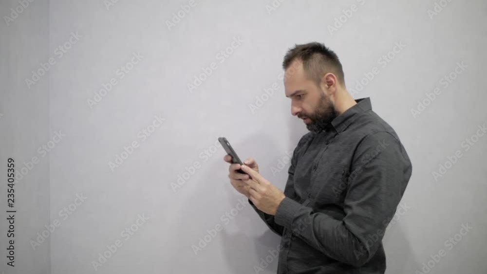 A man in a shirt and a beard writes SMS in the phone A man in a shirt and a beard writes SMS in the phone