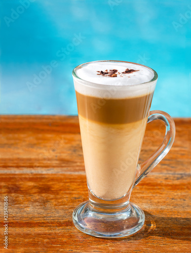 Glass of latte coffee drink on wooden table with defocus blue background.