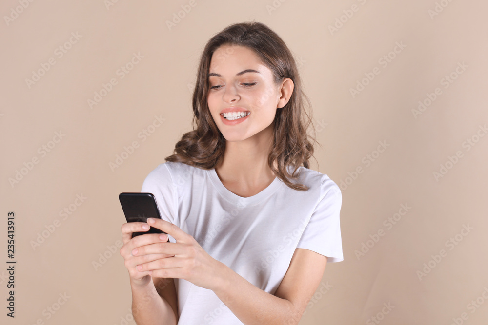 Young woman dressed in basic clothing isolated on beige background, using mobile phone. Young woman dressed in basic clothing isolated on beige background, using mobile phone.