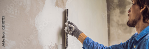 master is applying white putty on a wall and smearing by putty knife in a room of renovating house in daytime BANNER, long format photo