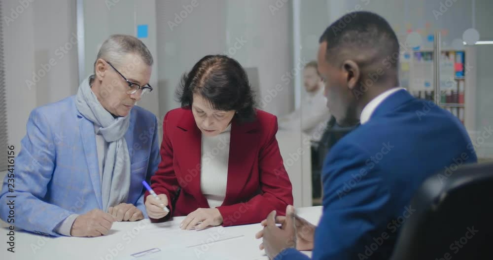 An elderly couple signing papers in a notary's office, An elderly couple signing papers in a notary's office,