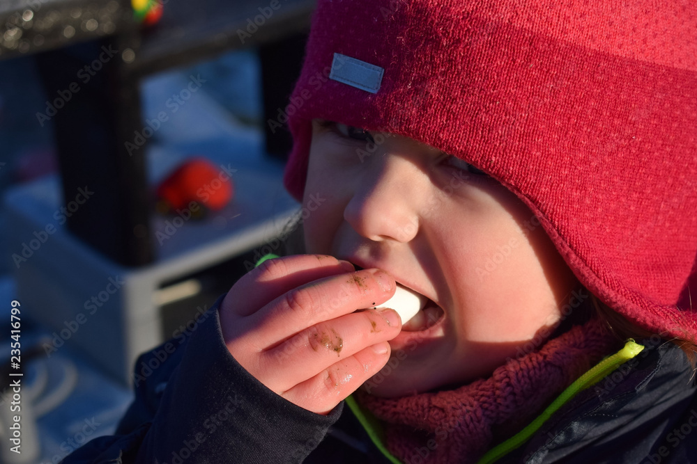A child in a red hat eats marshmallows. The face of the child close-up. Winter portrait of a girl with marshmallows.