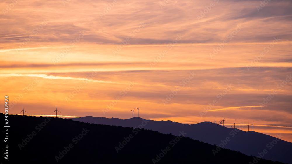 Side view of the silhouettes of mountain ranges at sunset time with wind generators on them. Greece