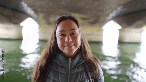 alone winsome brunette woman is smiling broadly standing under old stone bridge over river