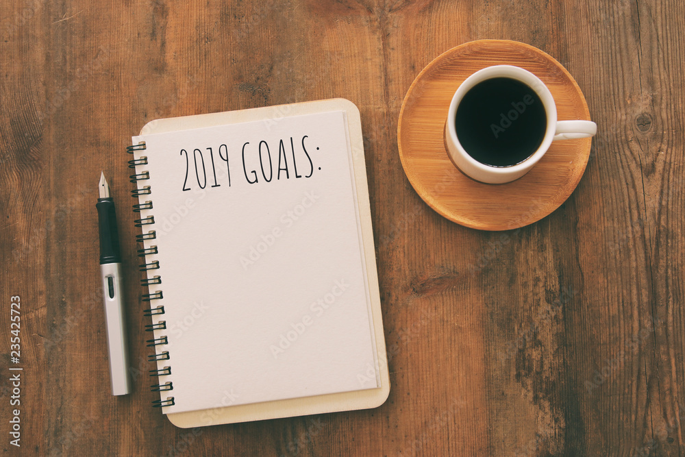 Top view image of 2019 goals list with notebook, cup of coffee over wooden desk. Top view image of 2019 goals list with notebook, cup of coffee over wooden desk.