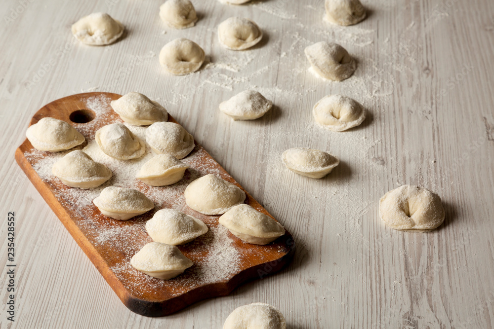 Homemade raw tortellini on white wooden surface, low angle view.