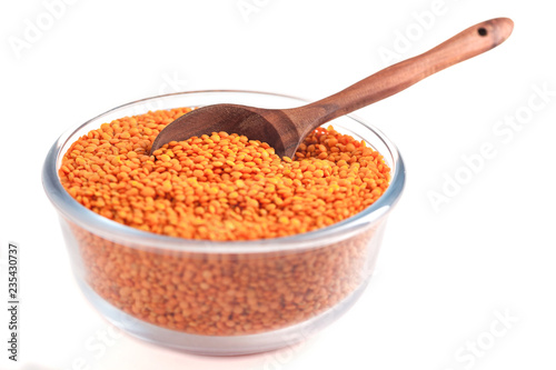 Yellow lentil in glass bowl with wooden spoon isolated on white background