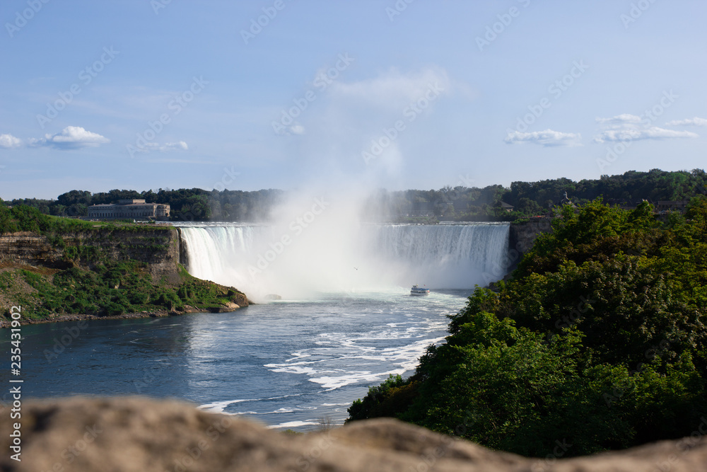 Wide view of the beautiful American side of the Niagara falls and a boat in front of it, from the Canadian side. Wide view of the beautiful American side of the Niagara falls and a boat in front of it, from the Canadian side.