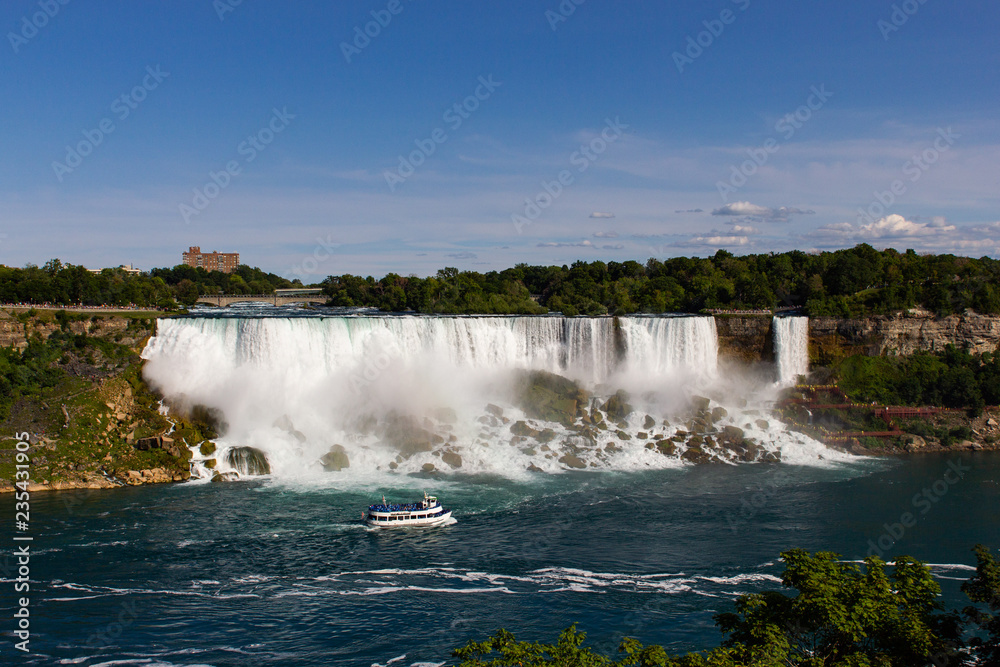 Wide view of the beautiful American side of the Niagara falls and a boat in front of it, from the Canadian side. Wide view of the beautiful American side of the Niagara falls and a boat in front of it, from the Canadian side.