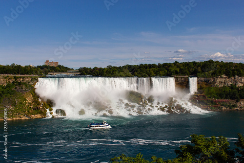 Wide view of the beautiful American side of the Niagara falls and a boat in front of it, from the Canadian side.