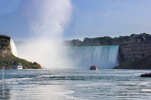 Wide view of the beautiful American side of the Niagara falls and a boat in front of it, from the Canadian side.