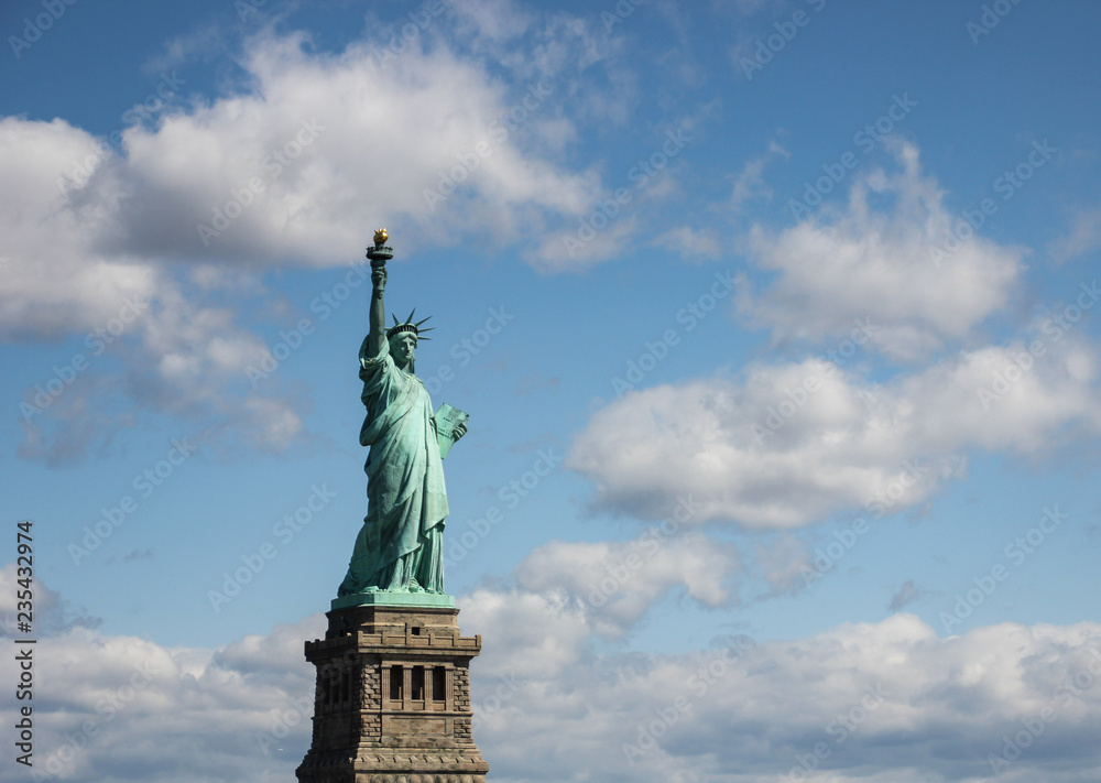 Statue of Liberty near New York city and Manhattan taken from a boat with a beautiful blue sky and some clouds in the background, United States