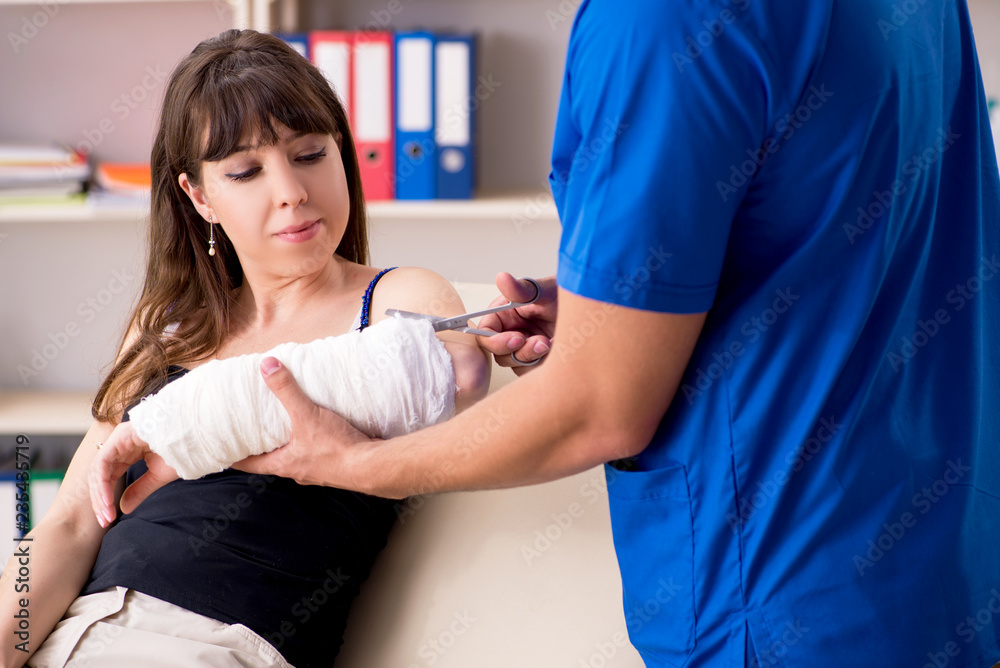 Obraz premium Young woman with bandaged arm visiting male doctor traumotologis