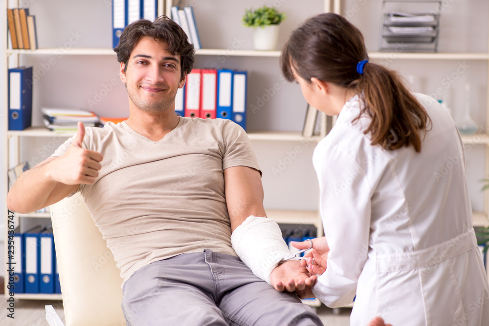 Young man with bandaged arm visiting female doctor traumatologis
