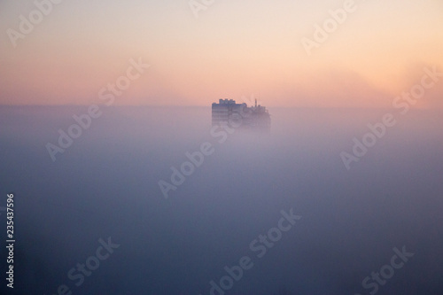 Buildings in morning haze. Panoramic view of misty city. Foggy cityscape. Scenic winter landmark. Sunrise and fog over city buildings. Aerial background. 