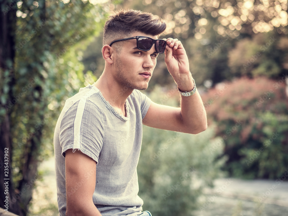 One handsome young man in urban setting in European city park, near a river One handsome young man in urban setting in European city park, near a river