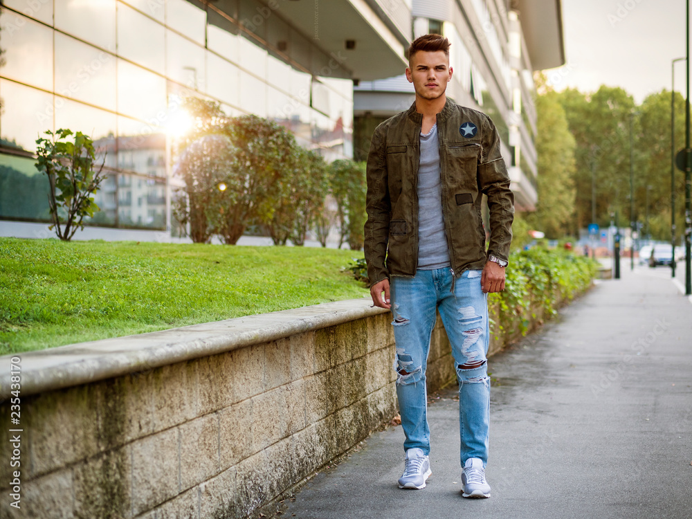 Fototapeta premium Handsome young man walking in city with backpack on shoulders, wearing t-shirt