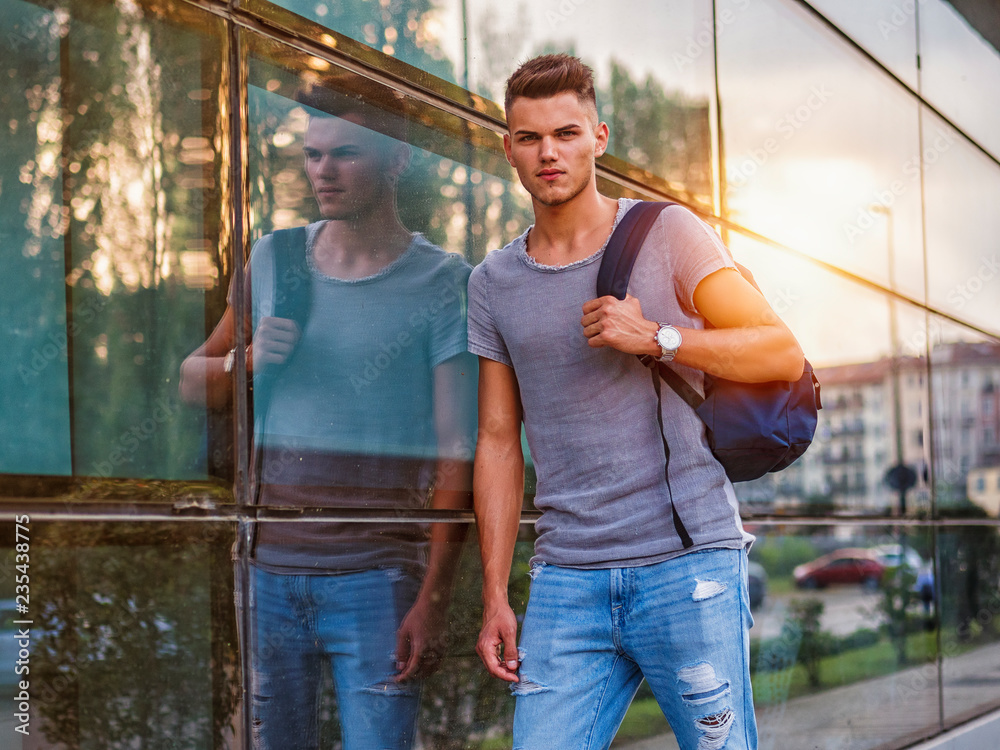 Handsome young man walking in city with backpack on shoulders, wearing t-shirt