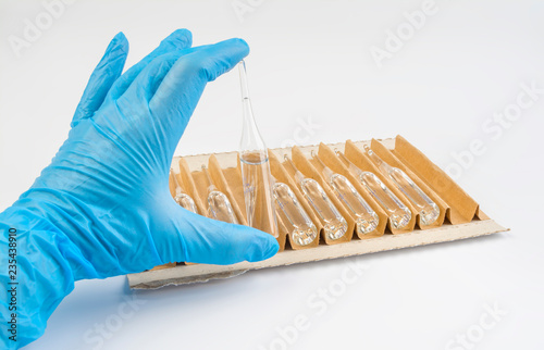 The doctor's hand in a blue glove holds the ampoule on a white background. photo