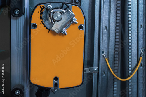 Orange damper actuator installed on the industrial ventilation unit body, front view