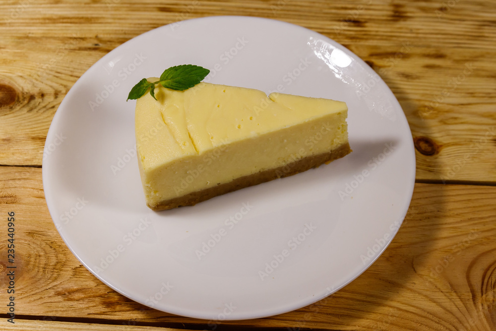 Piece of tasty sweet New York cheesecake in a white plate on wooden table