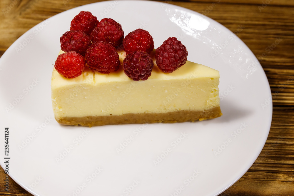 Piece of tasty New York cheesecake with raspberries in a white plate on wooden table Piece of tasty New York cheesecake with raspberries in a white plate on wooden table