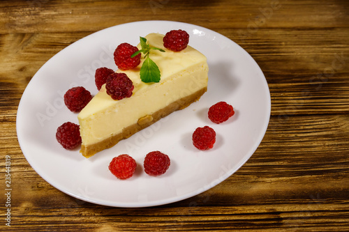 Piece of tasty New York cheesecake with raspberries in a white plate on wooden table