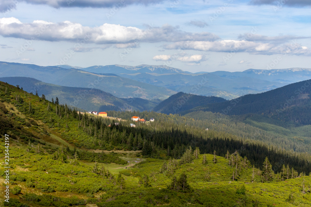 Panoramic mountains view with village and clouds shadow on green forest valley. Carpathian mountains in perspective. Majesic rural landscape in Carpathains, Ukraine. Beautiful sky with clouds.
