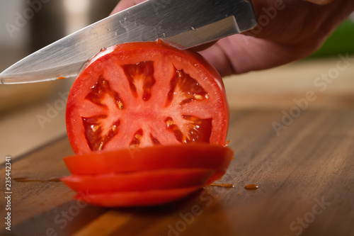 Closeup of slicing ripe tomato with knife on cutting board