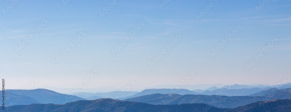 Blue mountains peaks panorama. Vastness and calmness concept. Clear blue sky over blue mountains on sunset. Mystical aerial panorama. Misty silhouettes of Carpathian mountains. Travel and tourism.