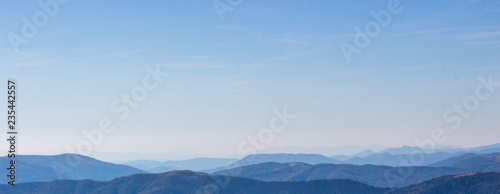 Blue mountains peaks panorama. Vastness and calmness concept. Clear blue sky over blue mountains on sunset. Mystical aerial panorama. Misty silhouettes of Carpathian mountains. Travel and tourism.