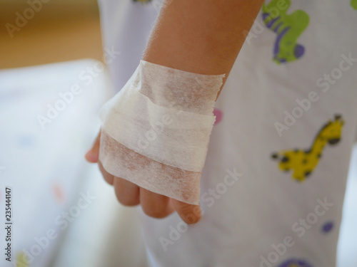 Little baby's hand covered with tape after applying cream for local anaesthesia, waiting to get numb before performing IV insertion