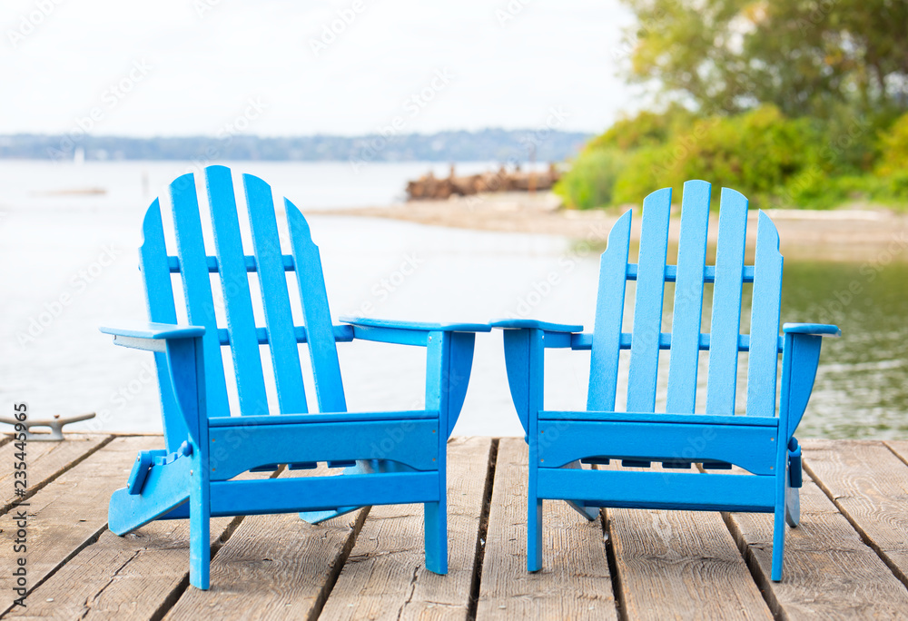 Blue adirondak chairs on wooden pier by lake in summer Blue adirondak chairs on wooden pier by lake in summer