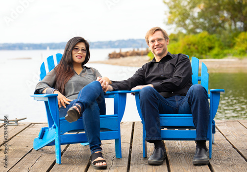Multiracial couple in late forties  on blue chairs by lake © Jaren Wicklund
