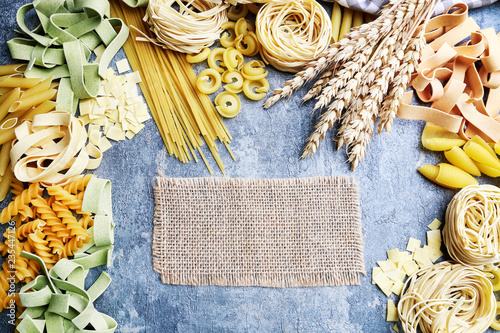 Mixed types and shapes of italian pasta on grey stone, background photo