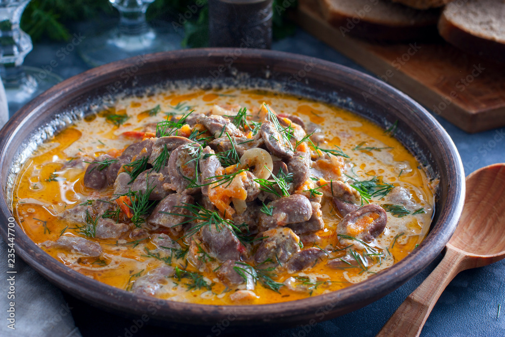 Chicken hearts stewed in sour cream in a clay bowl on a wooden stand, horizontal