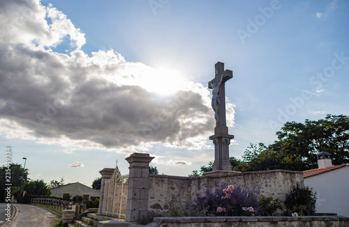 Statue Of Jesus On A Cross With Bright Sun Behind Clouds