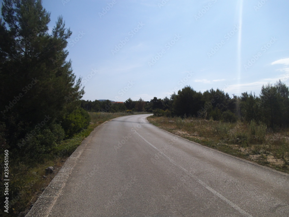 Obraz premium A street in the wildness in Sibenik. An asphalt street, scrub and trees are visible.