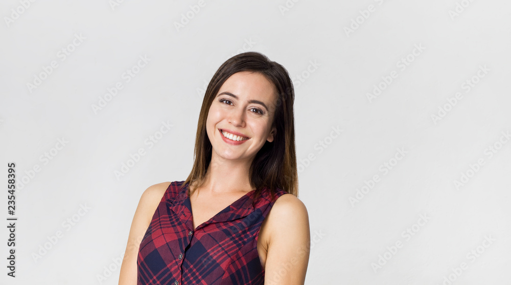 Smiling positive female with attractive look, wearing colorful dress, posing against white blank wall Smiling positive female with attractive look, wearing colorful dress, posing against white blank wall