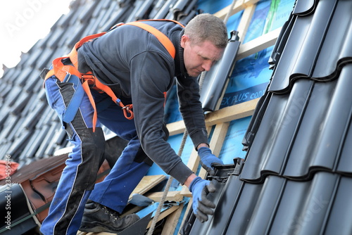Dachdecker Arbeiter auf Dachlatten stehend am Gurt beim Hausbau auf einer Immobilie, Reparatur und Dachdecker Arbeiten auf Baustellen mit erhöhter Arbeitssicherheit durch persönliche Schutzausrüstung photo