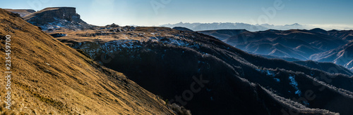 Panoramic landscape on Caucasus mountain range covered with snow and valley with yellow grass during autumn sunset