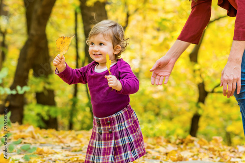 Happy Little Girl Learning to Walk with Mother Help in the Autumn Park