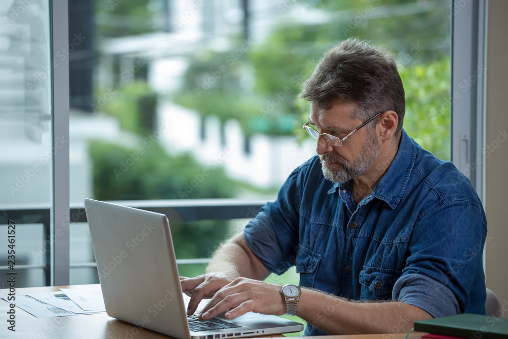 Caucasian man are working with a notebook in green blurred background.old man in coffee shop Caucasian man are working with a notebook in green blurred background.old man in coffee shop
