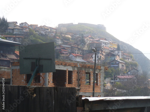 A bare brickwork house in Sarajevo. In the background is a hill with houses.
