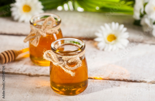 Glass jar of honey with wooden drizzler and chamomile